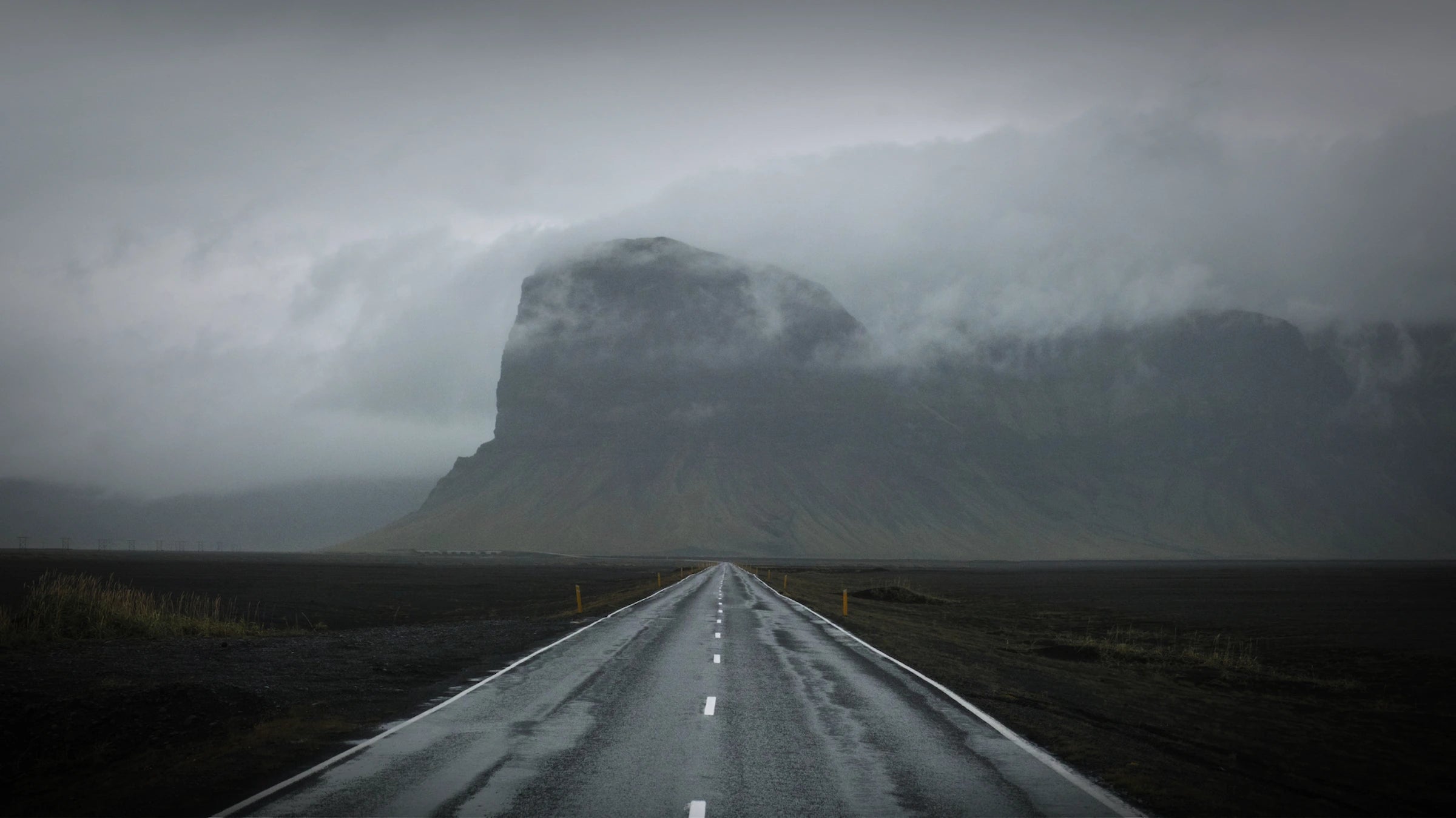 Route traversant un paysage de montagne minéral sous ciel couvert, Islande.